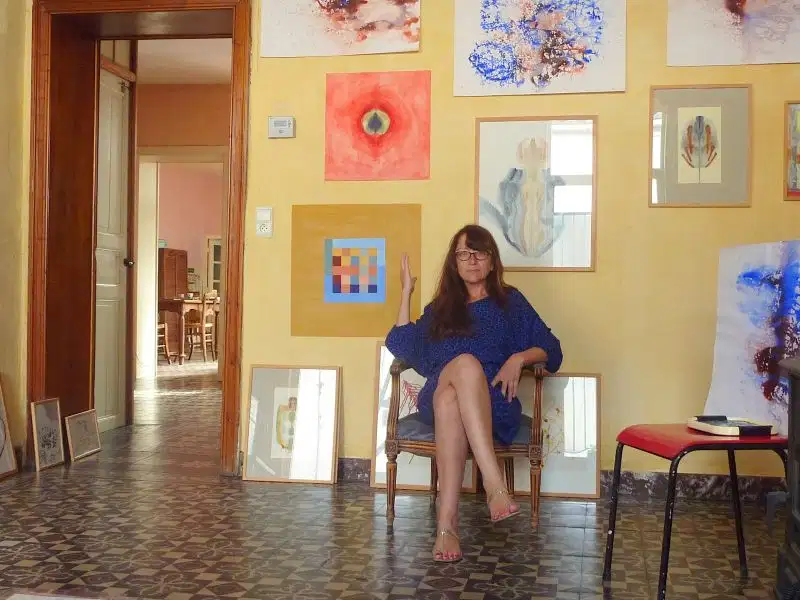 Lysiane Bourdon assise au milieu de ses peintures dans sa maison atelier